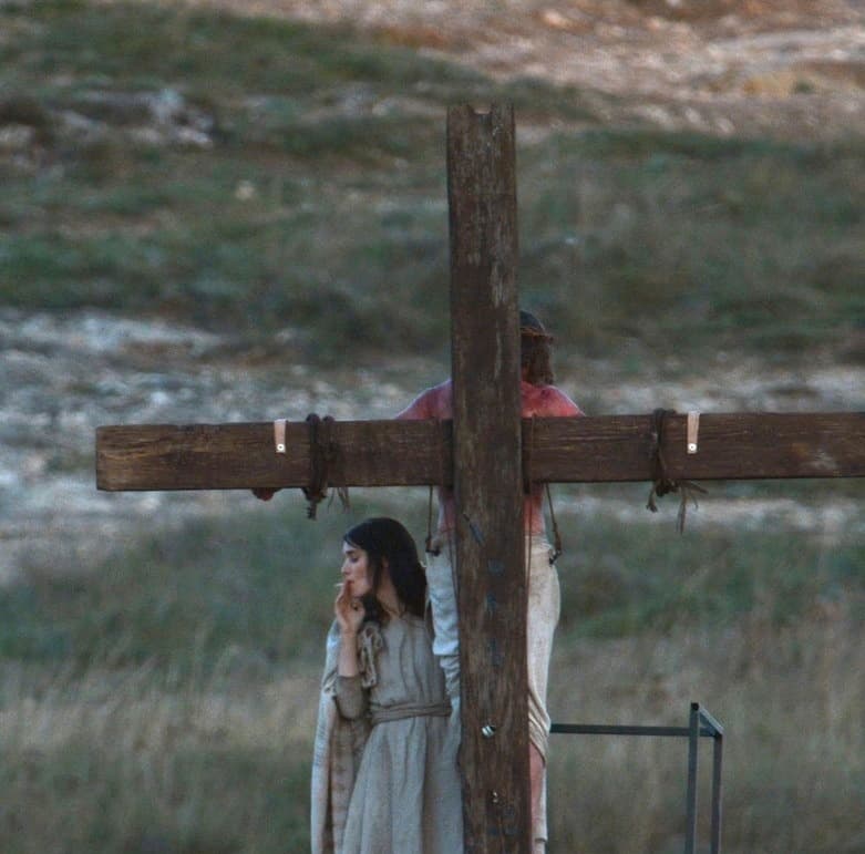 십자가에 매달린 예수 뒤편에서 한 여인이 담배를 피우고 있다